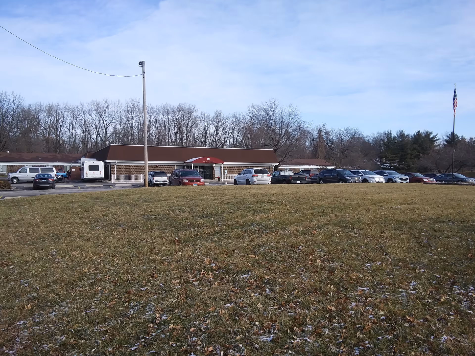 Front exterior of Evercare at University: single-story building, parking lot, flagpole, bare trees.