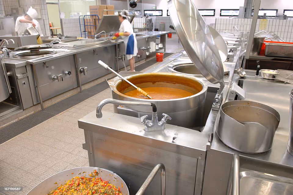 Industrial kitchen in a senior facility with large stainless pots and staff cooking.