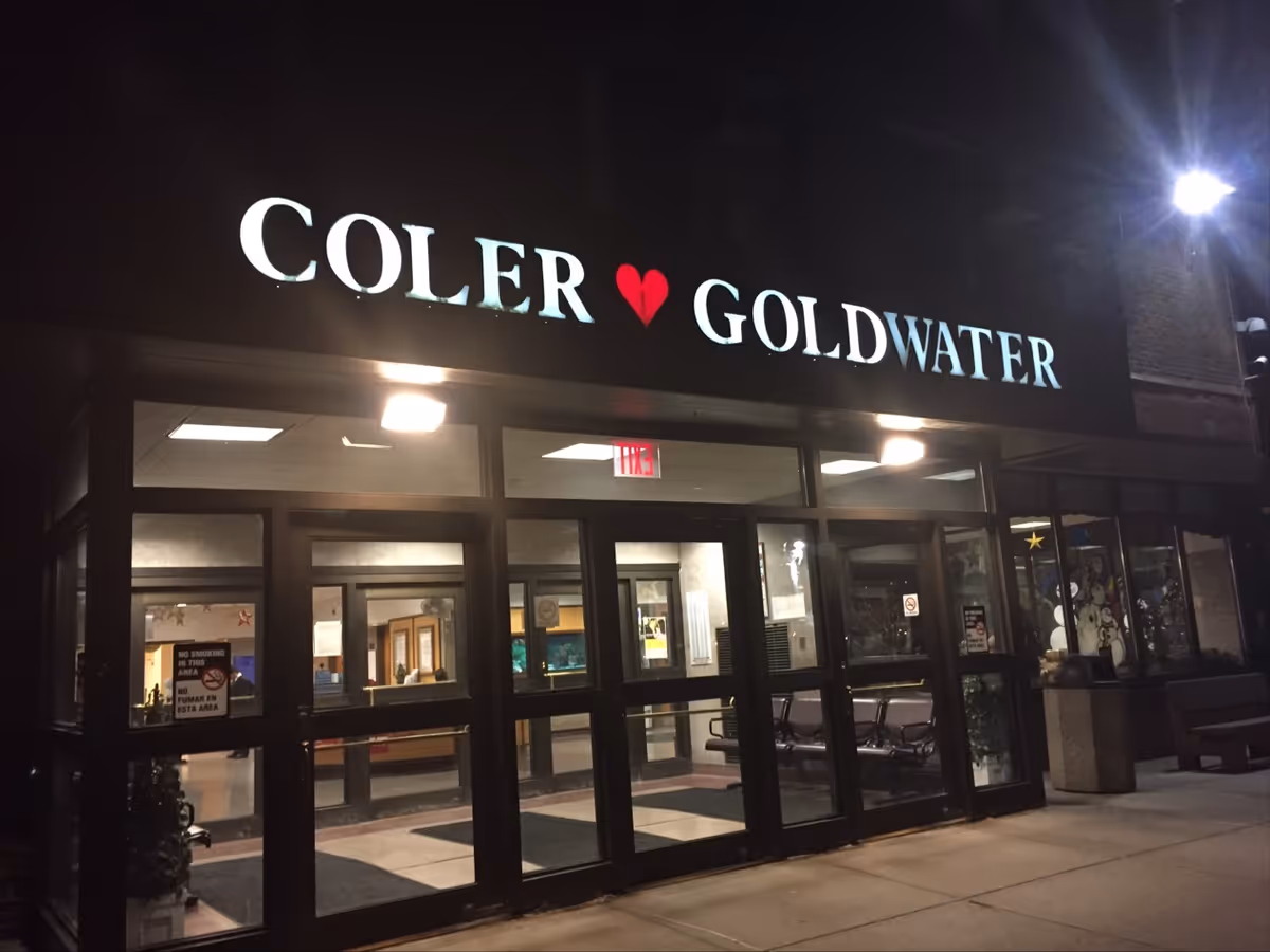 Night exterior of Coler Goldwater building with glass entry doors and a lobby in view.