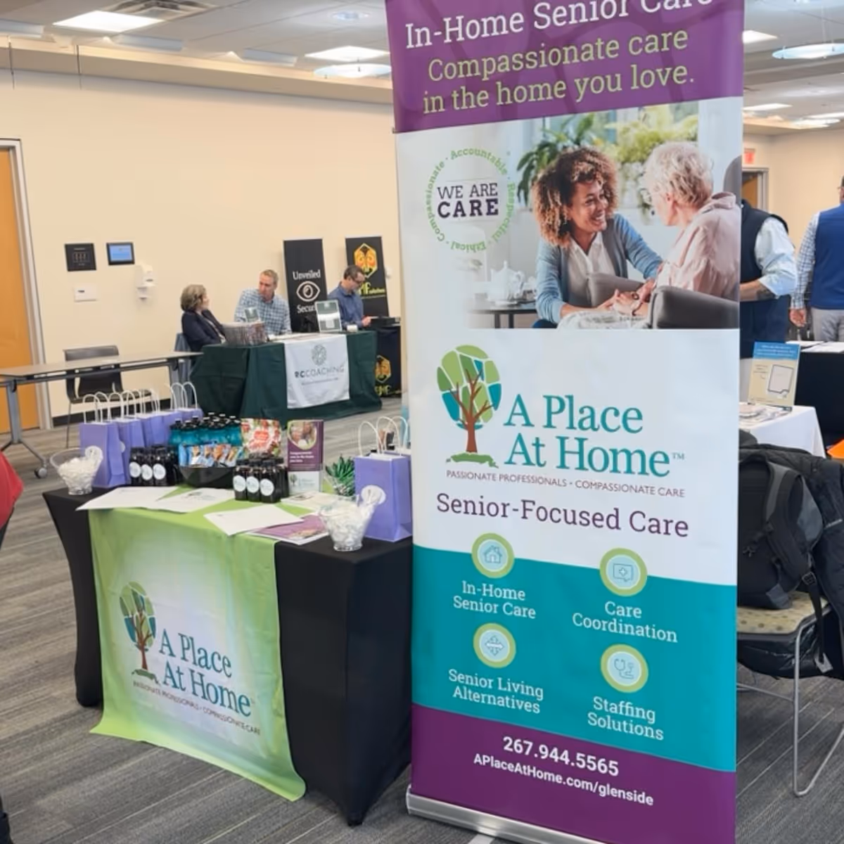 Indoor expo booth for A Place At Home Glenside with banners, tables, and materials.