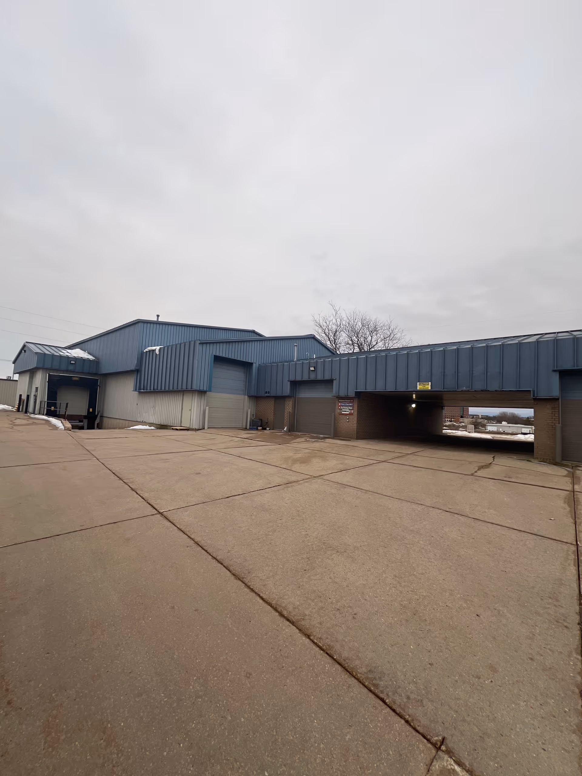 Exterior view of a blue industrial building with loading bays and a wide paved lot.