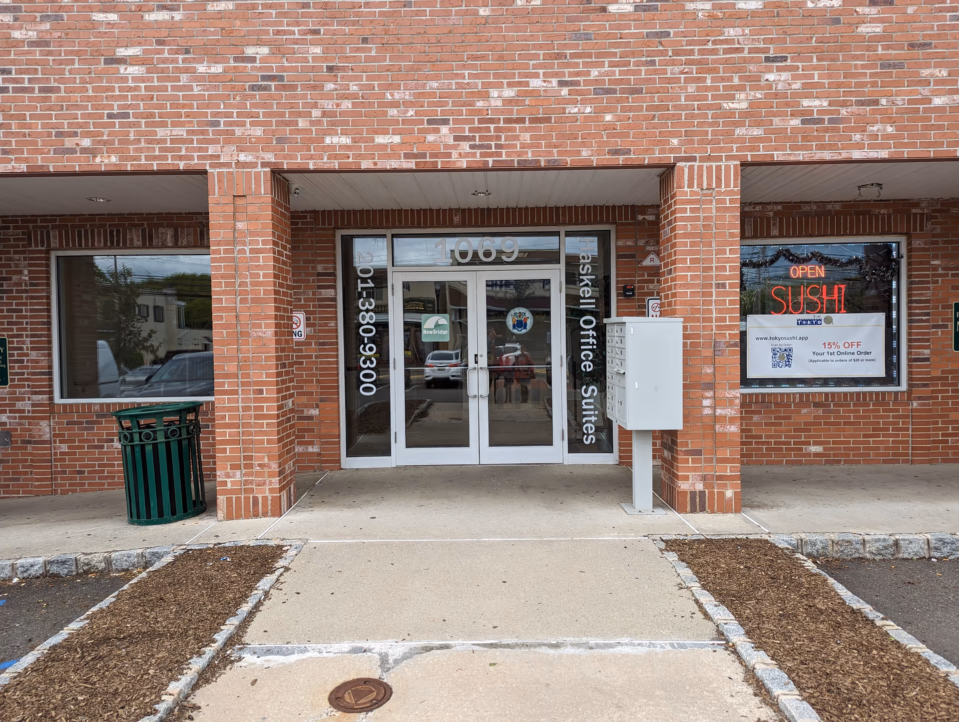 Brick building exterior featuring glass doors, sushi shop window, and a sidewalk walkway.