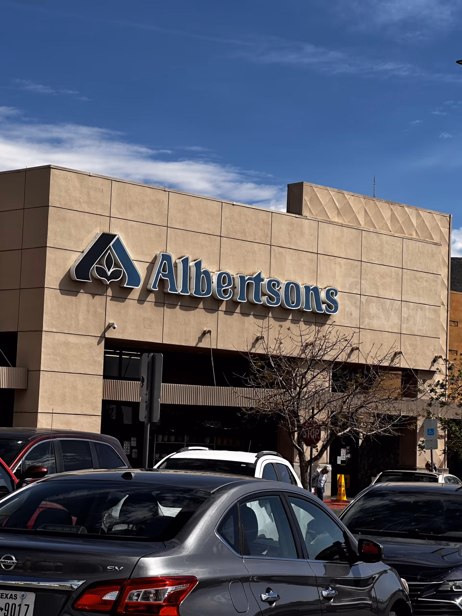 Albertsons storefront with a blue sign and parked cars in a parking lot.