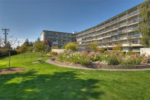 Well-maintained lawn, flower garden, and benches in front of a multi-story senior living building.
