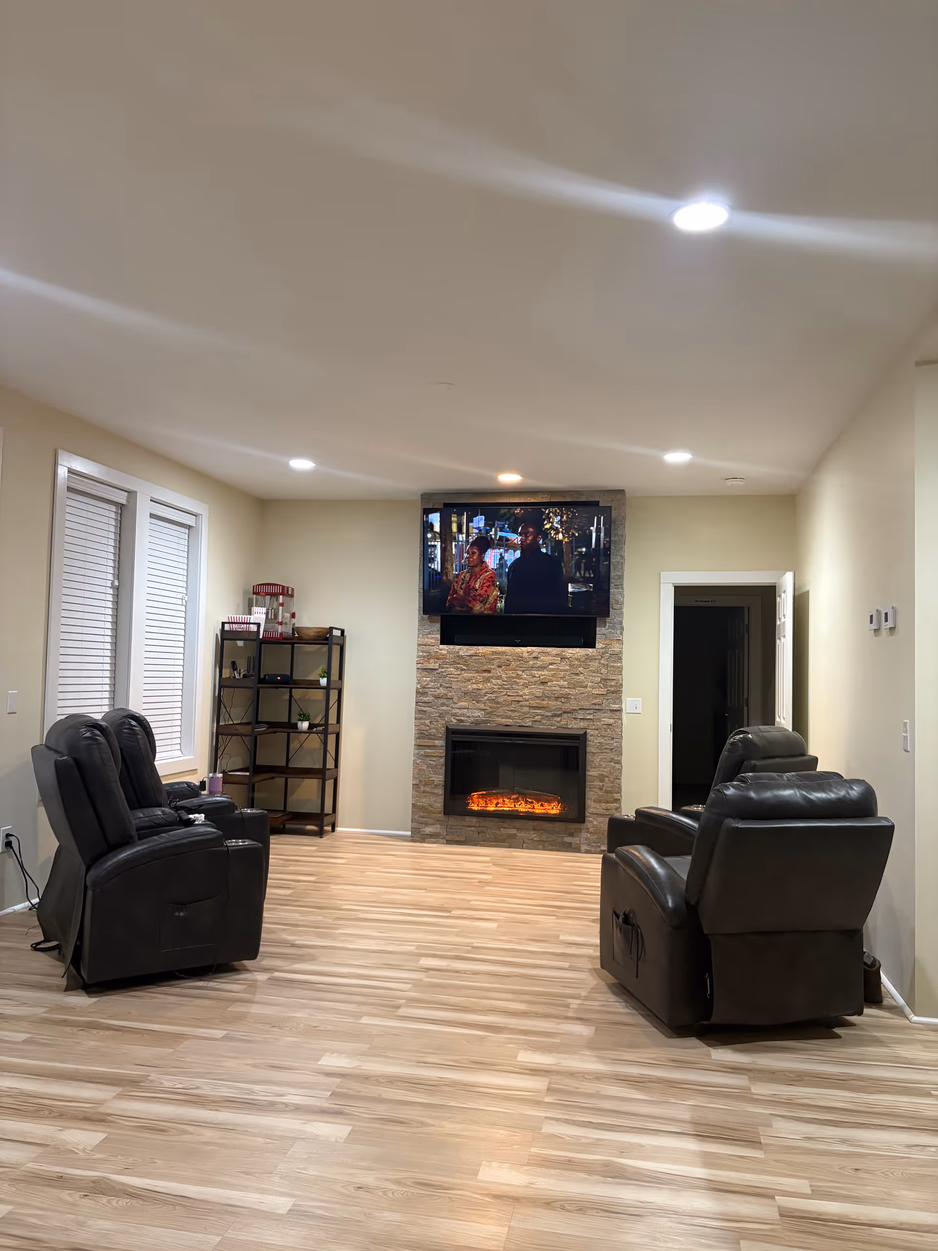 Cozy living room with recliners, a TV above a stone fireplace, and wooden floors.