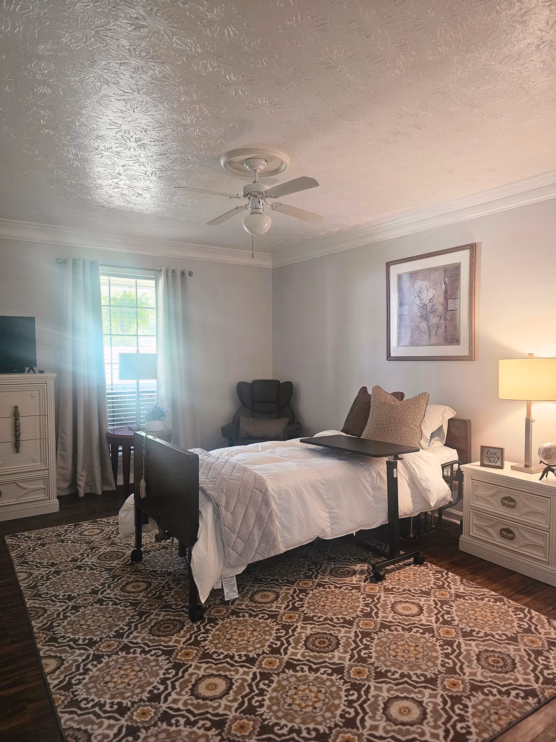 Bright bedroom with a bed, nightstands, dresser, and patterned rug.