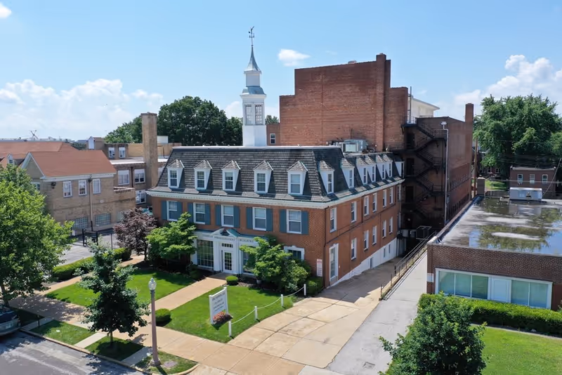 Front view of a brick senior care facility with a white steeple and lawn.