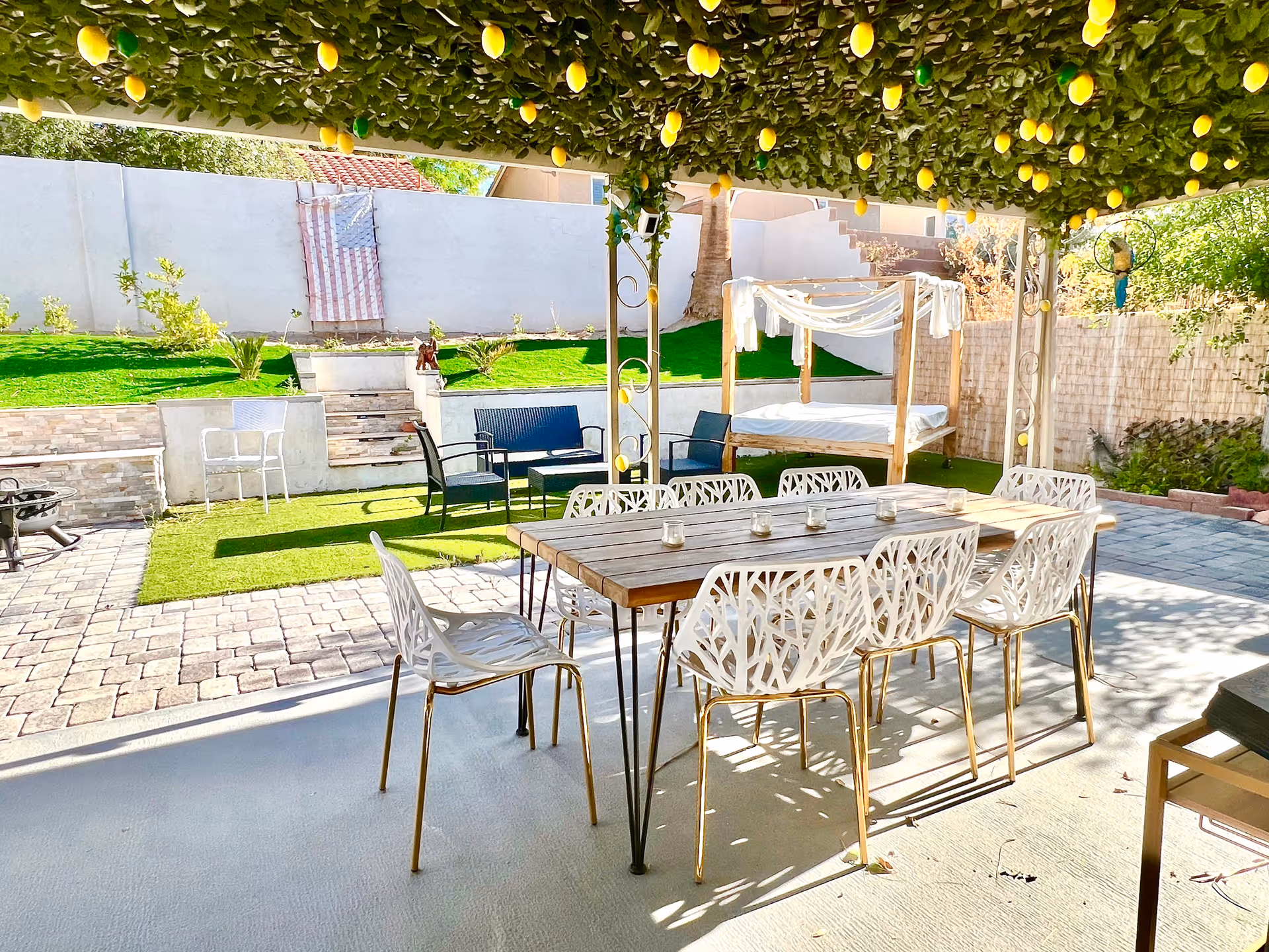 Outdoor garden patio with a long wooden dining table and white chairs.