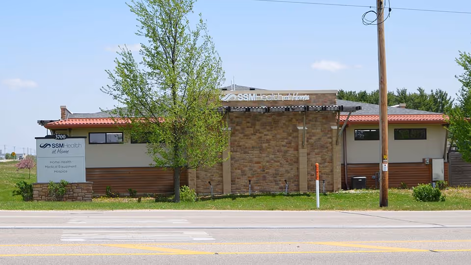 Exterior view of SSM Health at Home facility with trees and a sign in front.