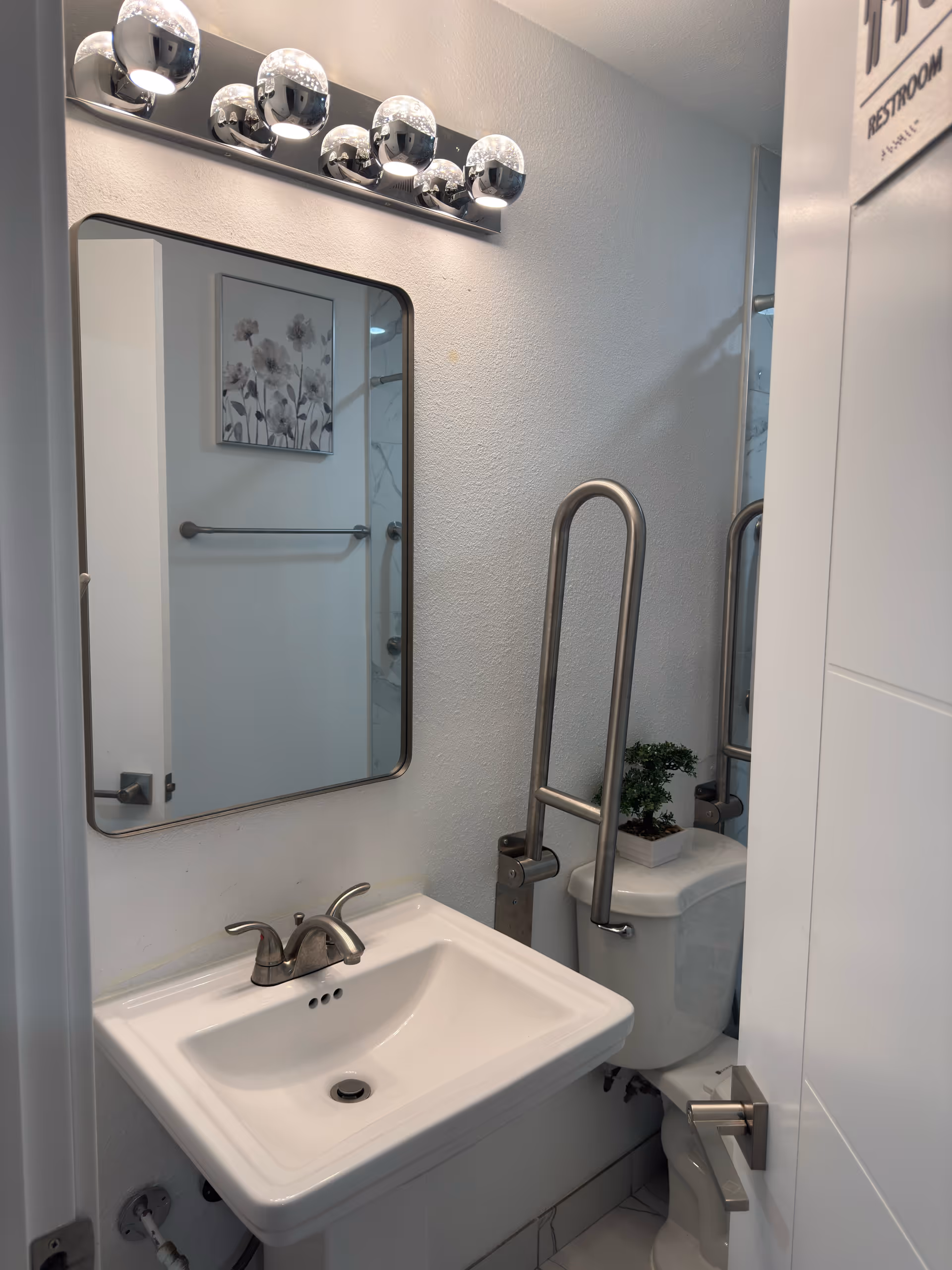 Small bathroom with sink, mirror, toilet, and grab bars.