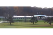 A long white senior living facility building sits in a grassy, tree-lined landscape.