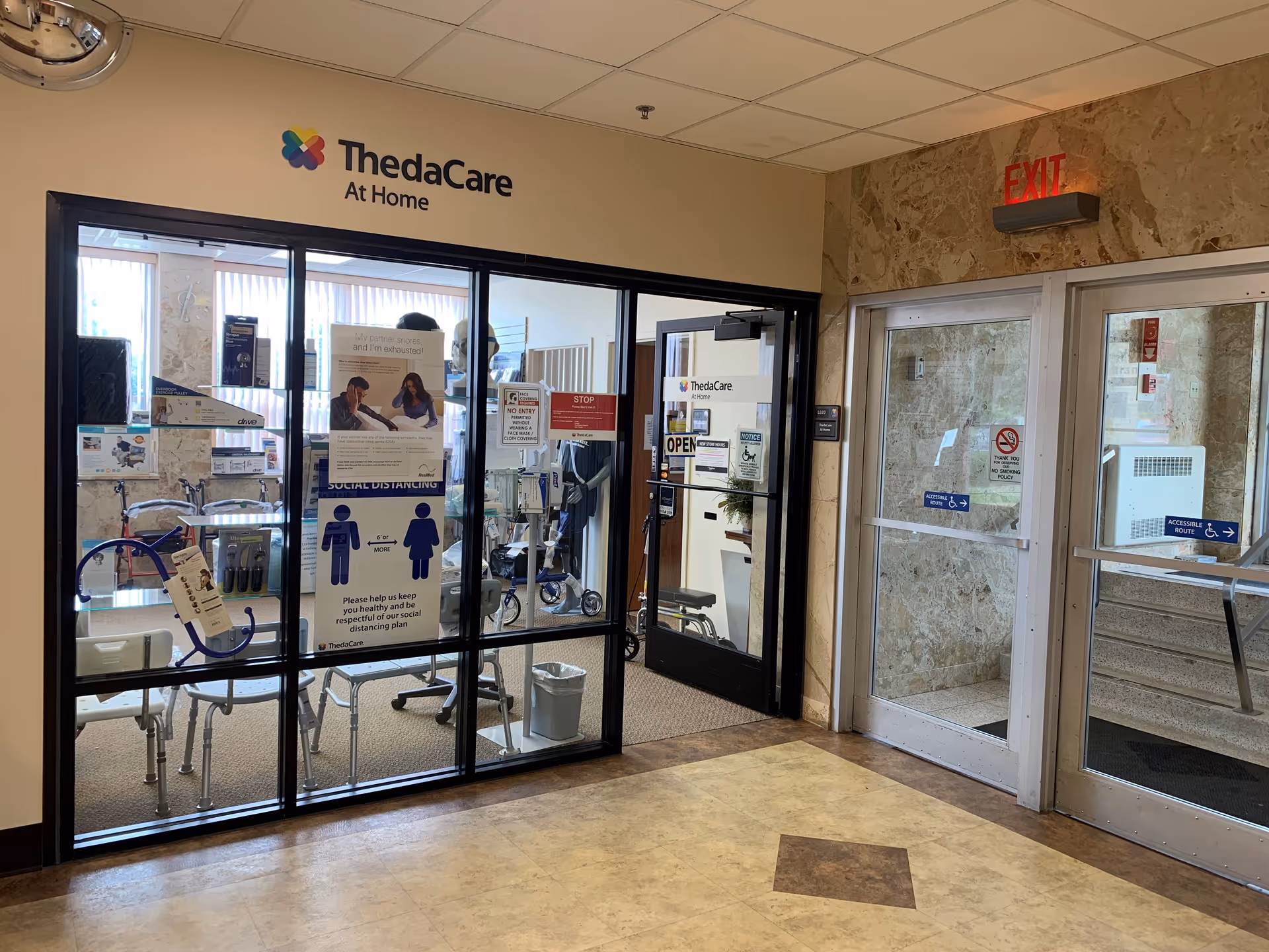 Interior entrance to ThedaCare At Home, glass doors, medical equipment, and informational posters visible.