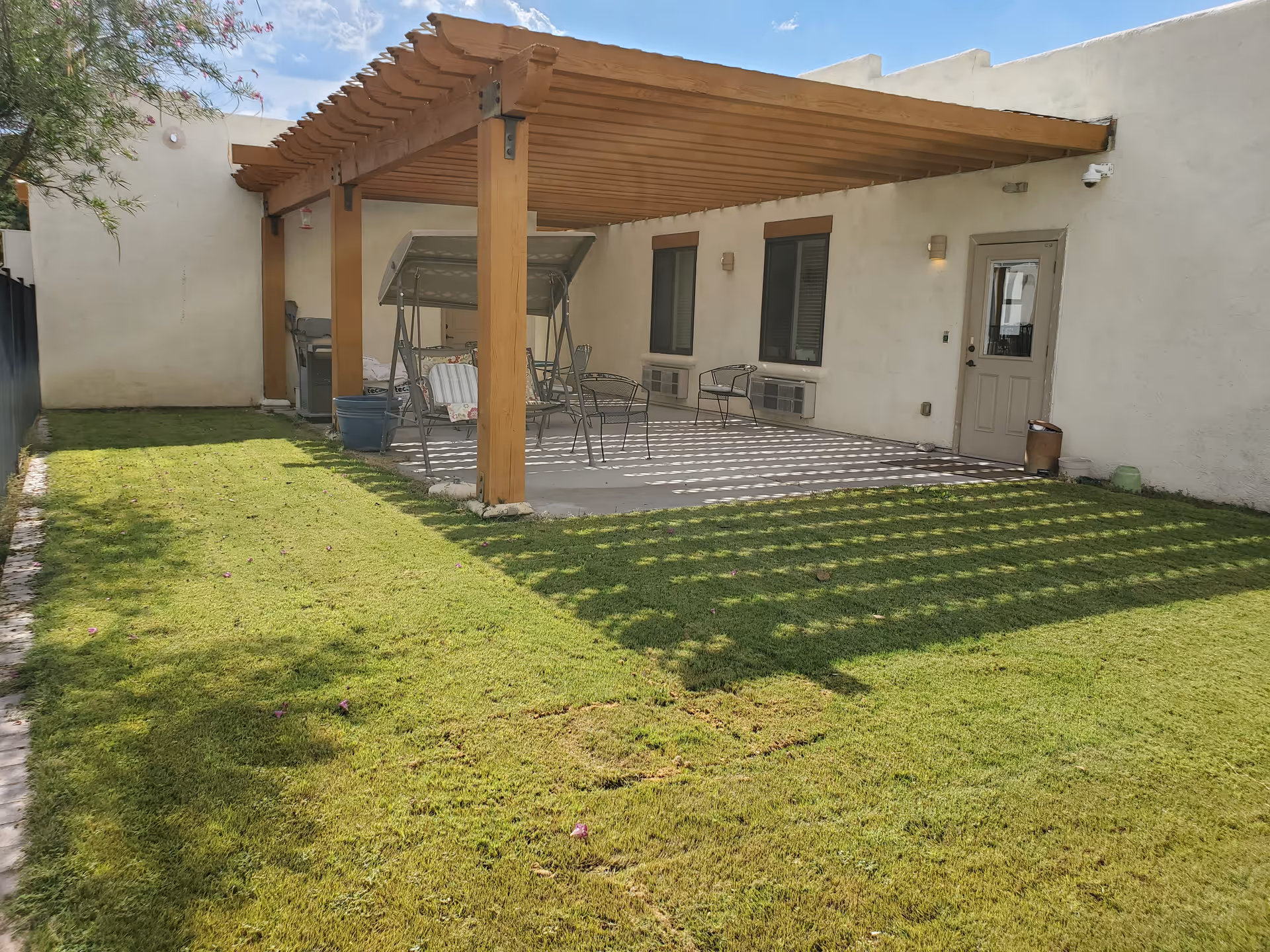 Backyard patio with wooden pergola, seating area, and a door to the facility