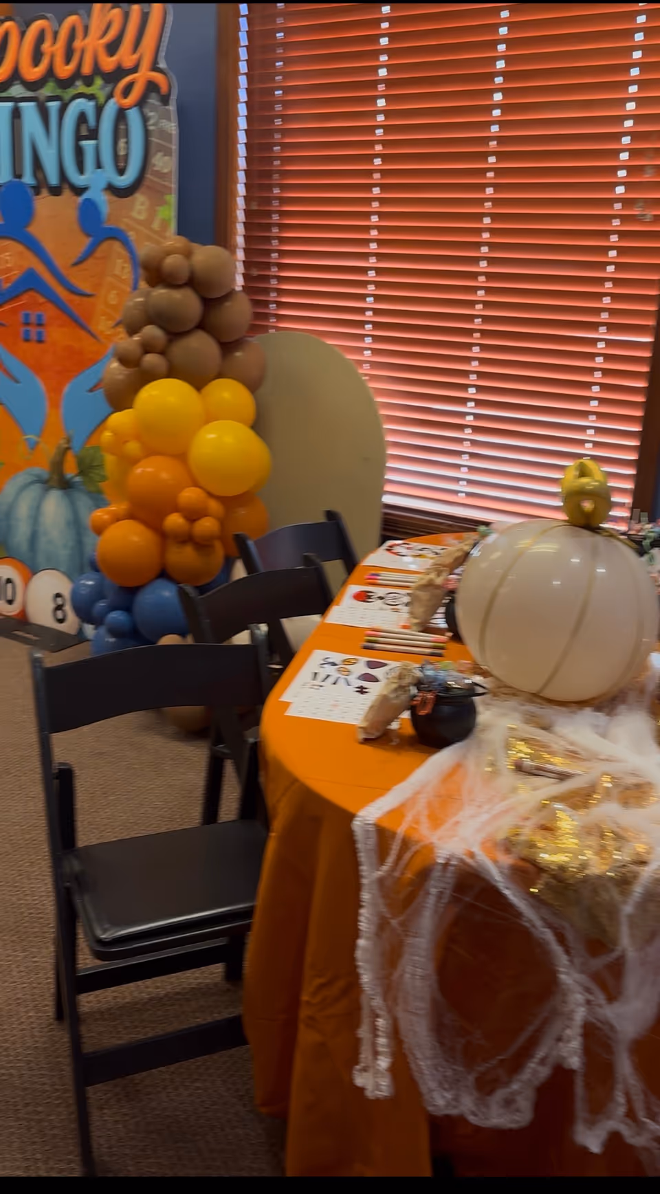 Interior dining room with Halloween table setup, pumpkins, balloons, and a spooky bingo backdrop.
