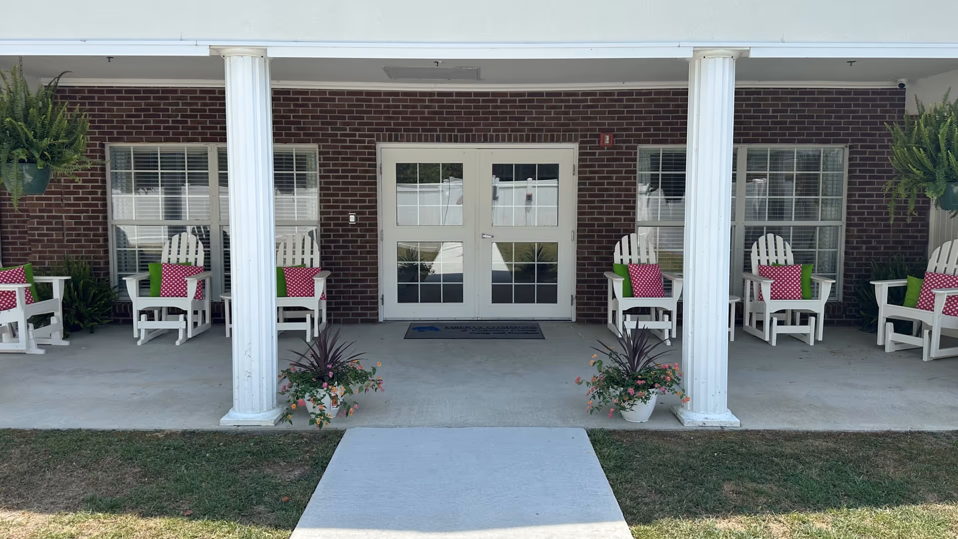 Front porch seating area with white Adirondack chairs, colorful cushions, and glass double doors.
