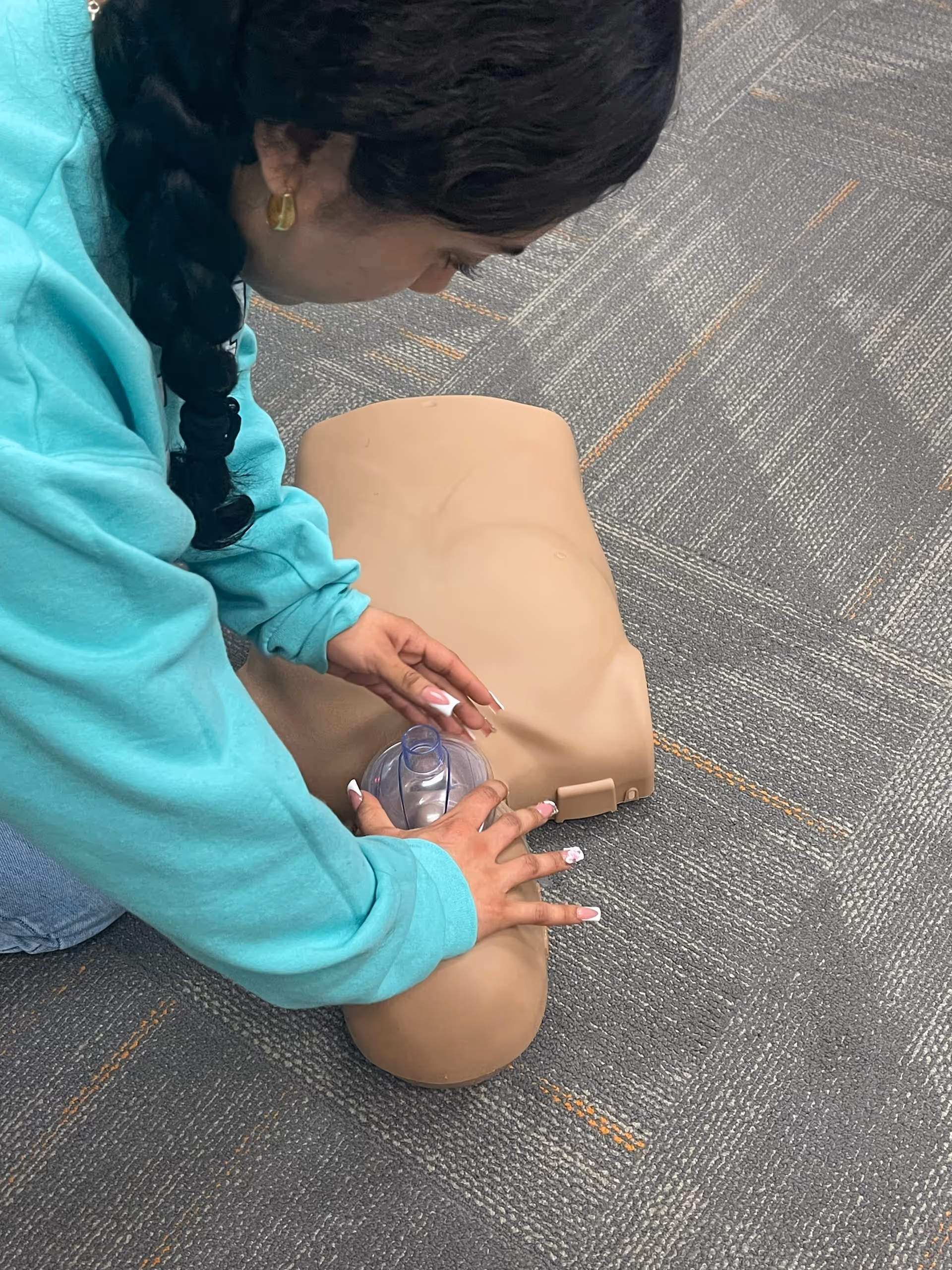 Person practicing CPR on a medical training mannequin indoors on carpet.