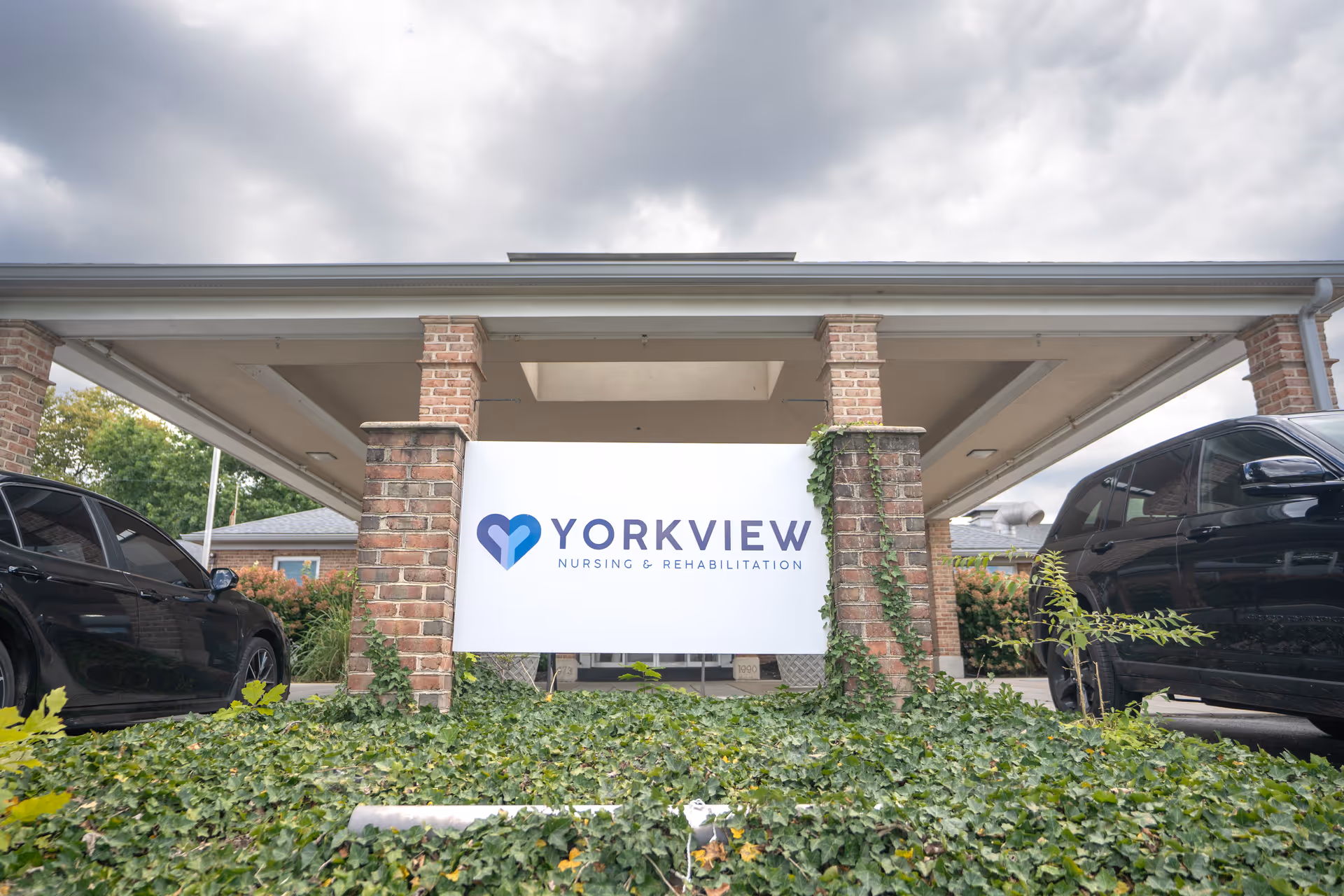 Exterior view of Yorkview Nursing & Rehabilitation entrance with brick pillars and cars.