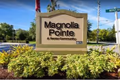 Magnolia Pointe Senior Community sign framed by shrubs on a sunny outdoor street scene.