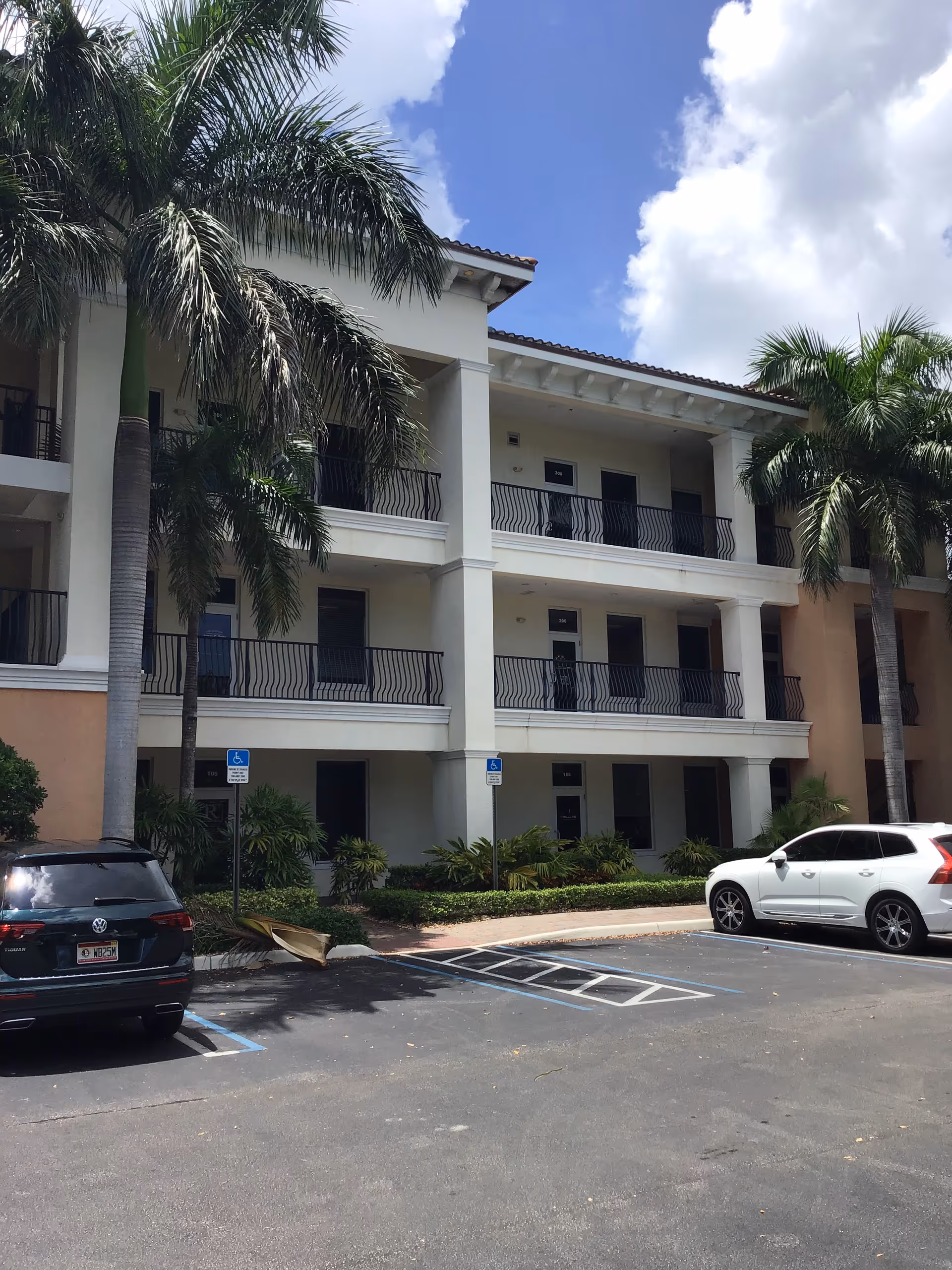 Exterior view of a multi-story senior living building with balconies and palm trees.