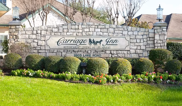 Stone entrance wall with Carriage Inn sign, shrubs, and a manicured lawn.