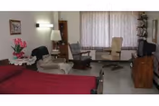 A furnished senior care room with a red bed, seating, and windowed curtains.
