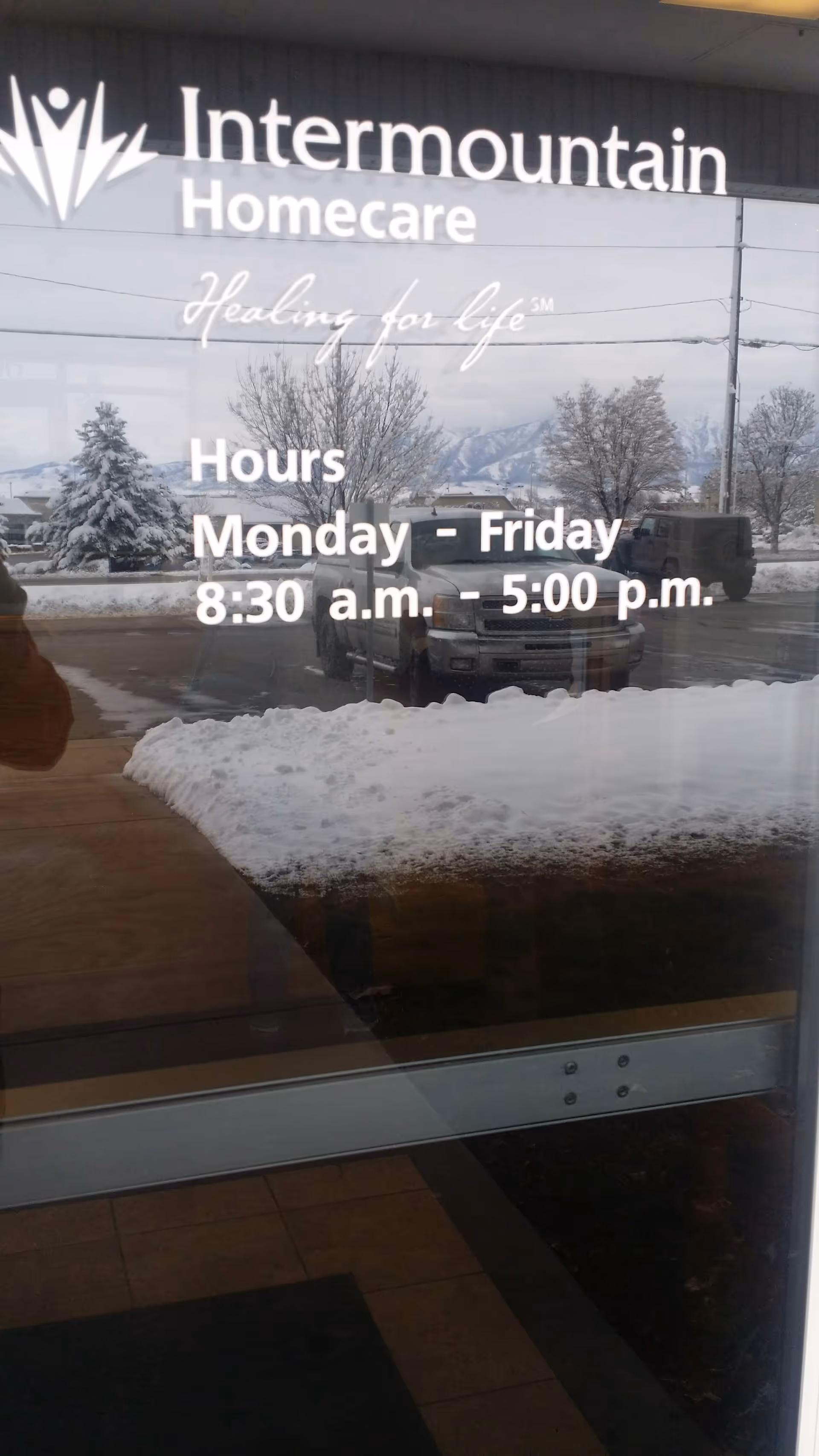 Glass storefront door showing Intermountain Homecare signage with snowy outdoor reflection.