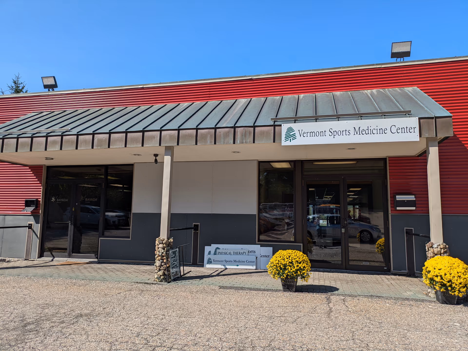 Front of a red building with metal awning, glass doors, and Vermont Sports Medicine Center sign.