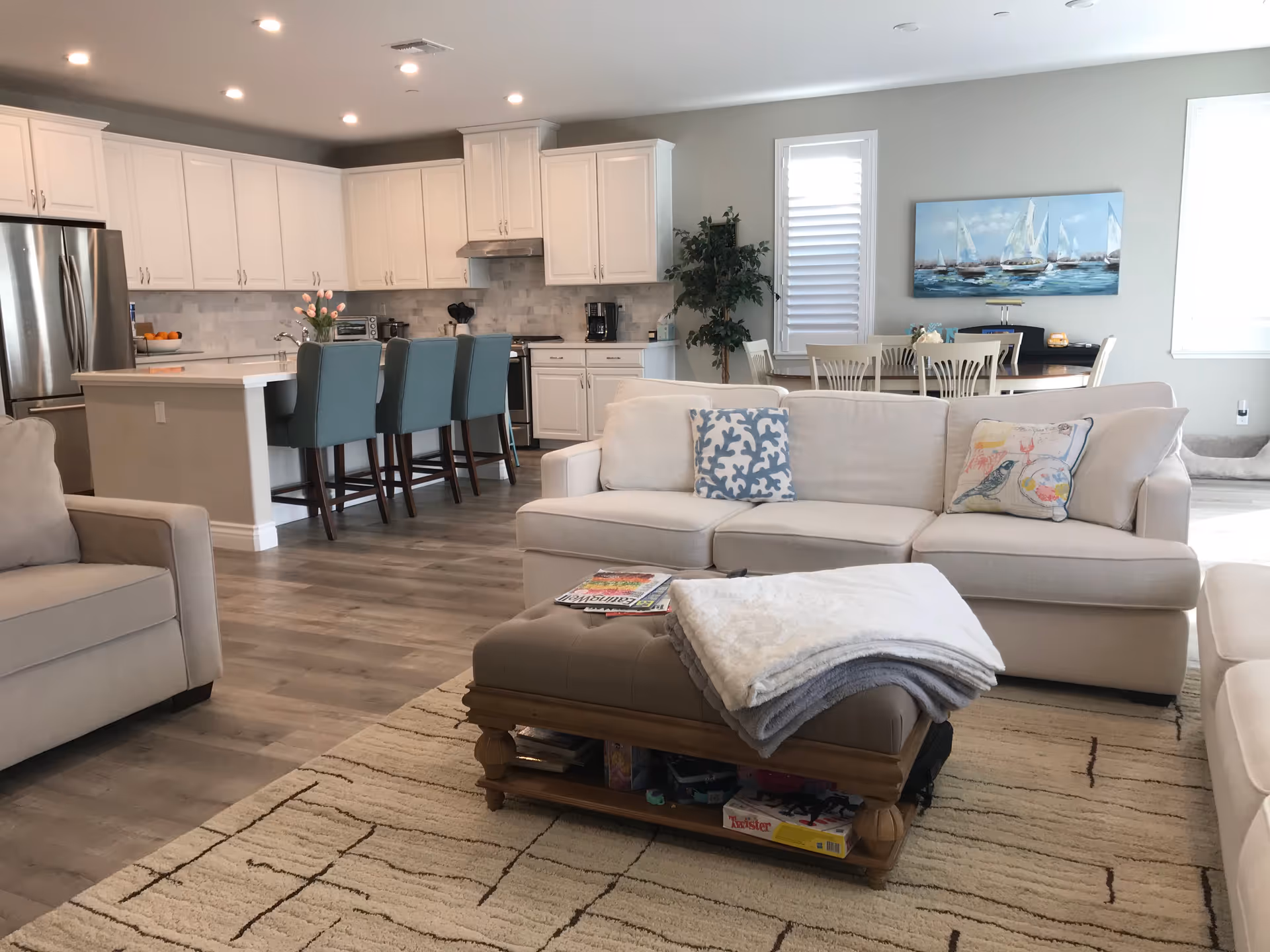 A bright open concept living area with white sofas, a kitchen island, and dining nook.