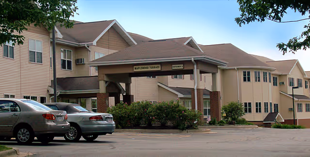 Front entrance and parking area of a beige multi-story senior living building with a covered drive-through labeled "Maplewood Terrace."