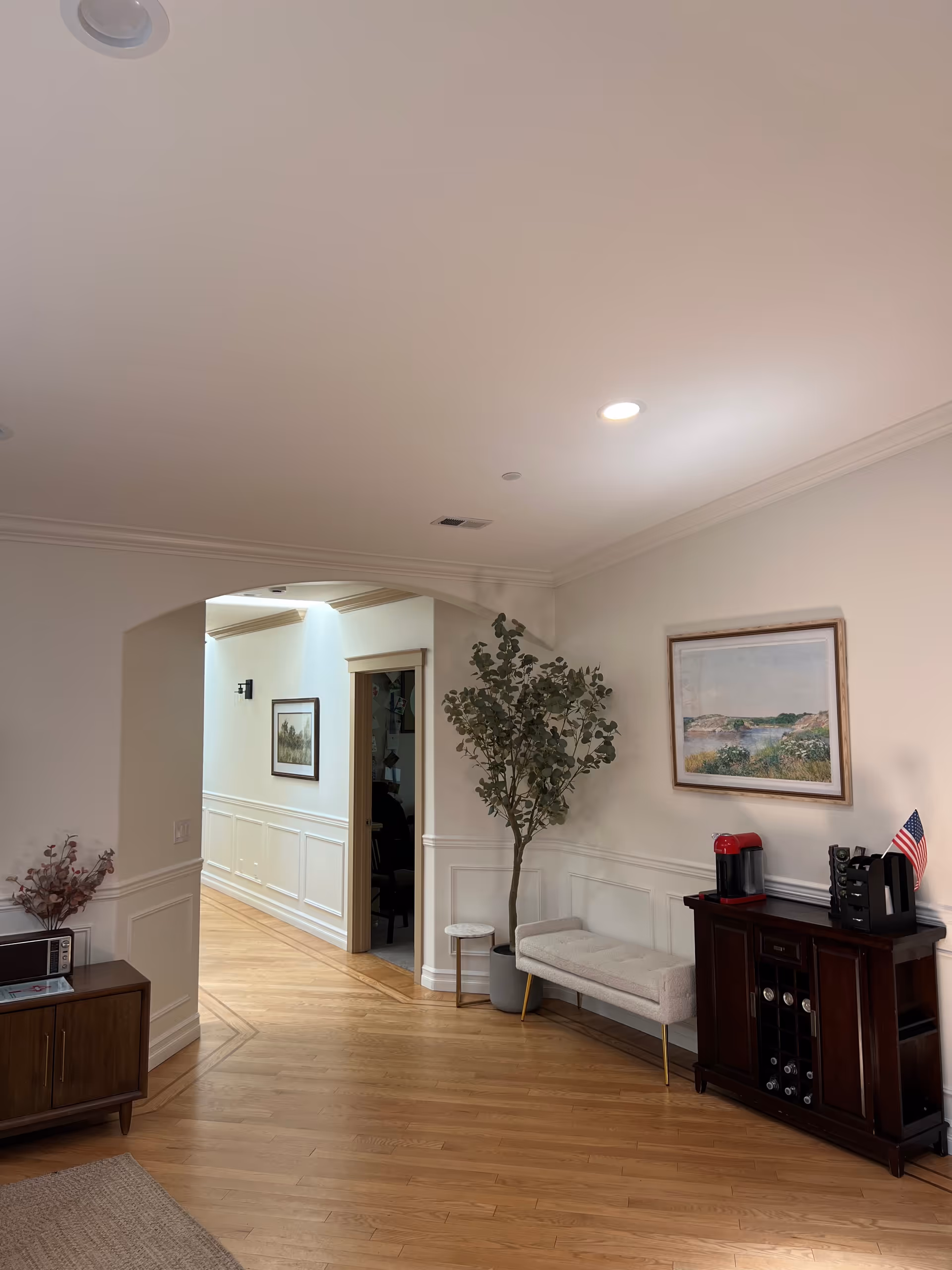 Interior lobby with hardwood floor, plant, bench, arch doorway, and coffee station.