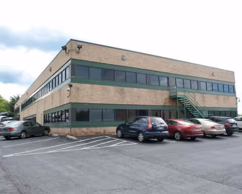 Two-story brick building with green trim, parking lot, and external staircase.