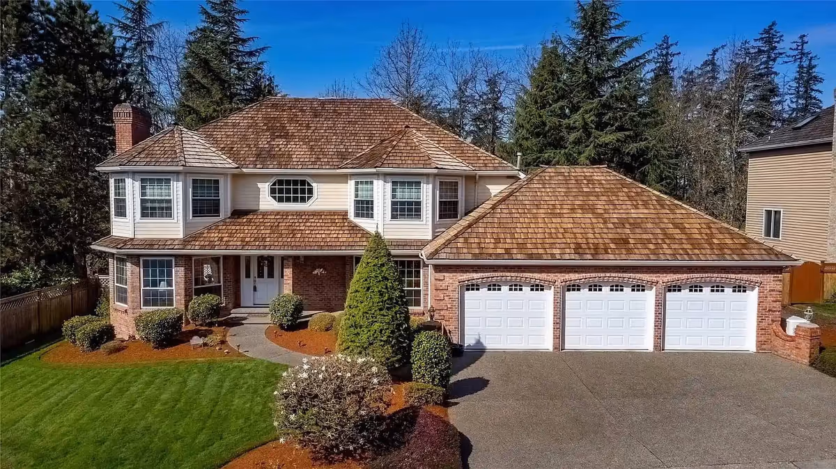 Two-story brick residence with beige siding, a three-car garage, and a manicured front yard.