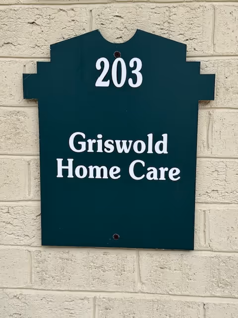 Dark green house-shaped sign on a beige brick wall reading '203 Griswold Home Care'.