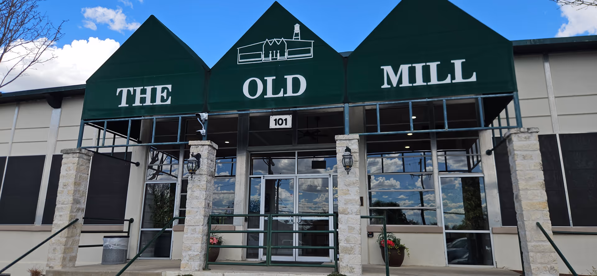 Front entrance of a building with a green awning reading THE OLD MILL and glass doors.