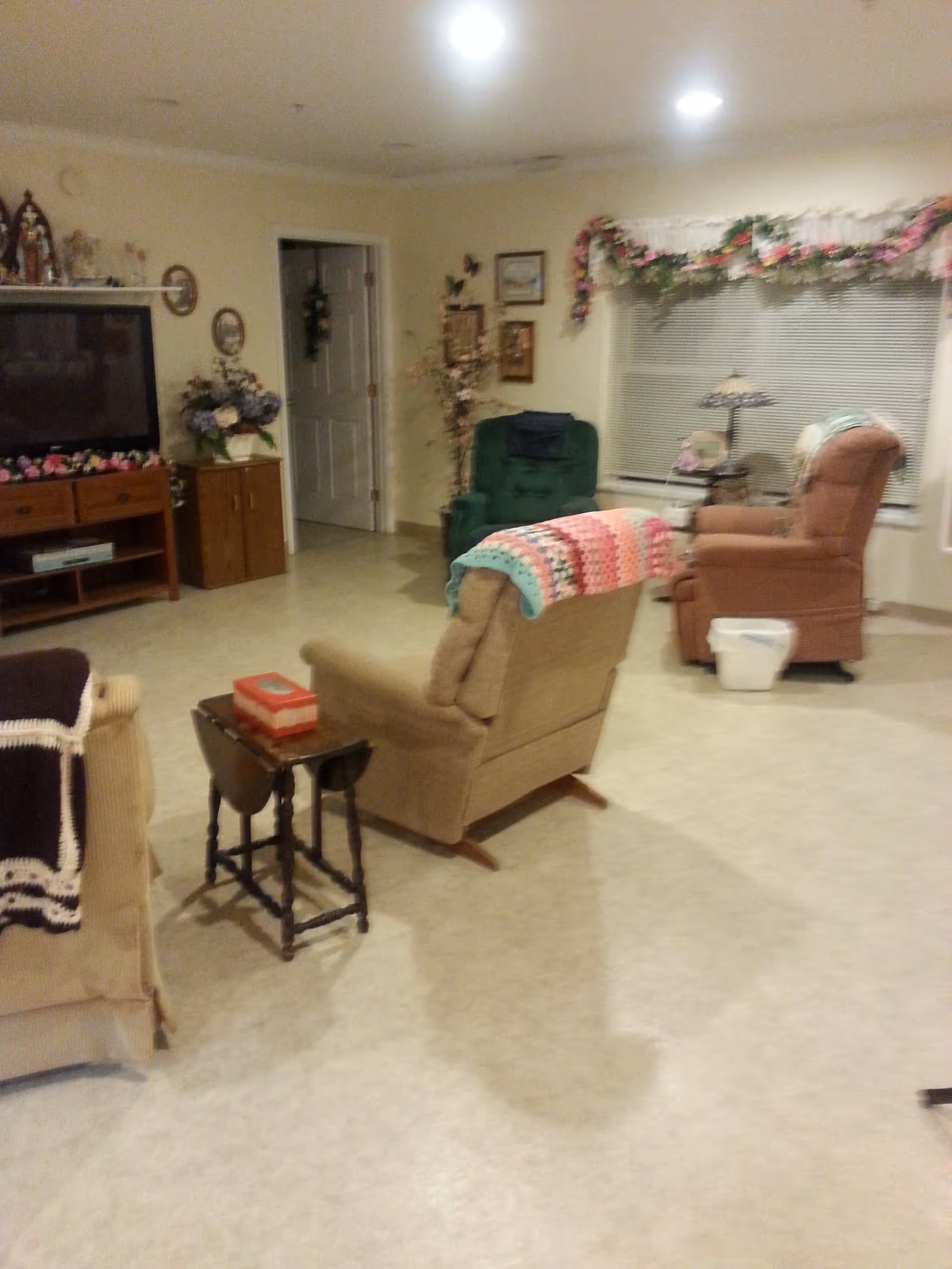 Cozy living room with several armchairs and recliners, a TV stand, side tables, and floral decorations.