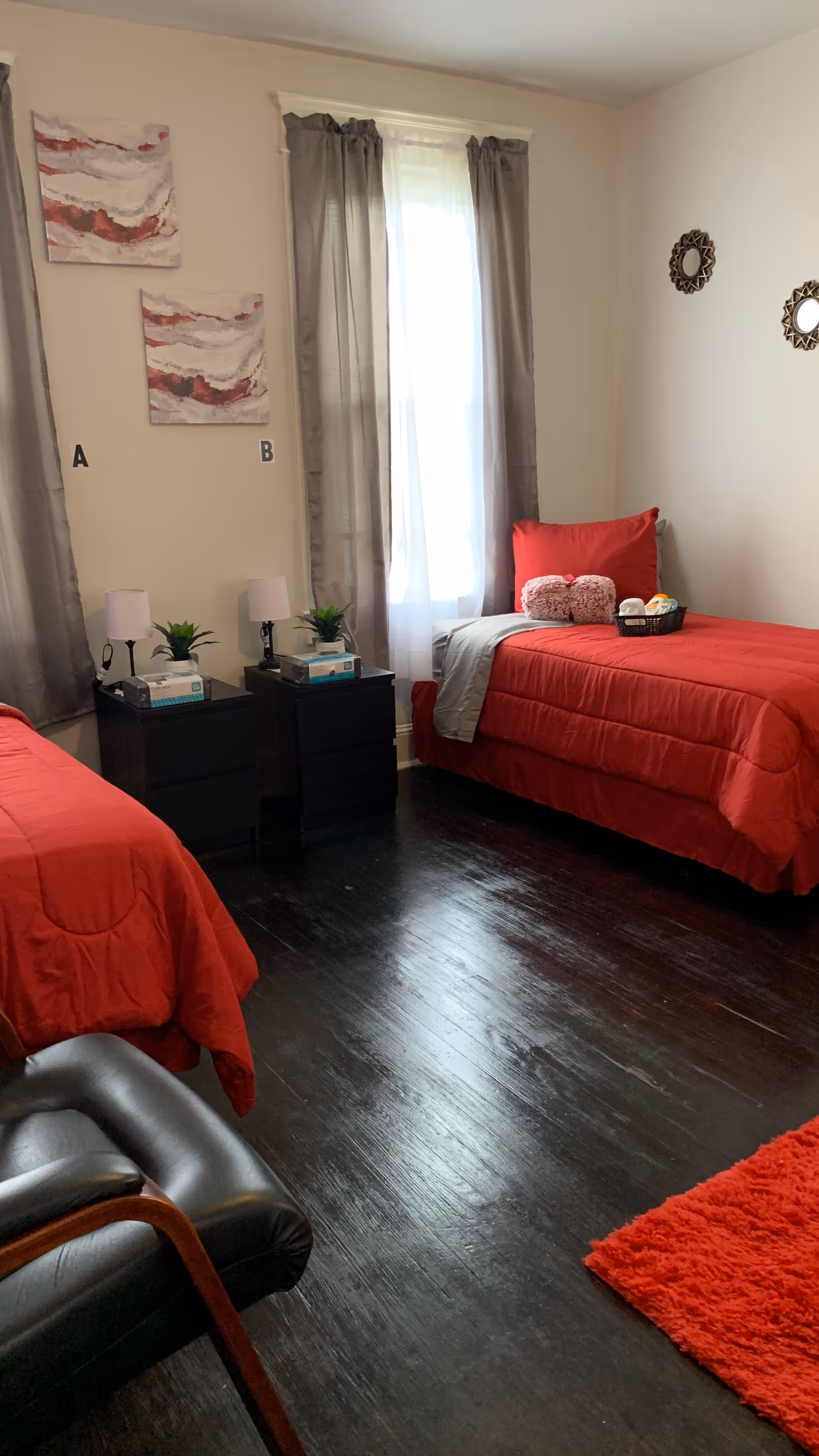 Two twin beds with red bedding, nightstands, lamps, and windows in a shared bedroom.