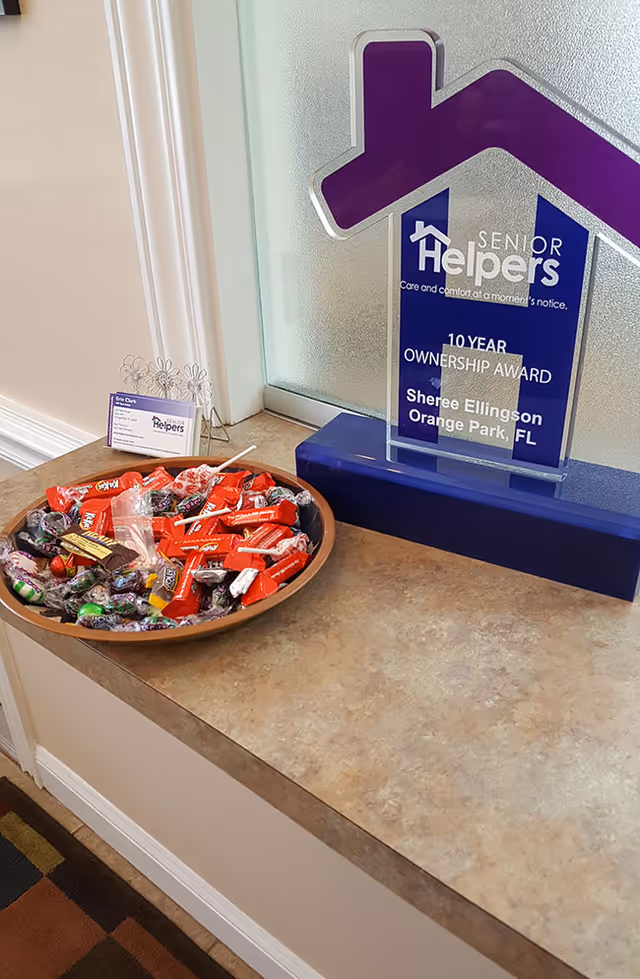 Candy bowl and award plaque on a counter beside a house-shaped Senior Helpers West Jacksonville logo