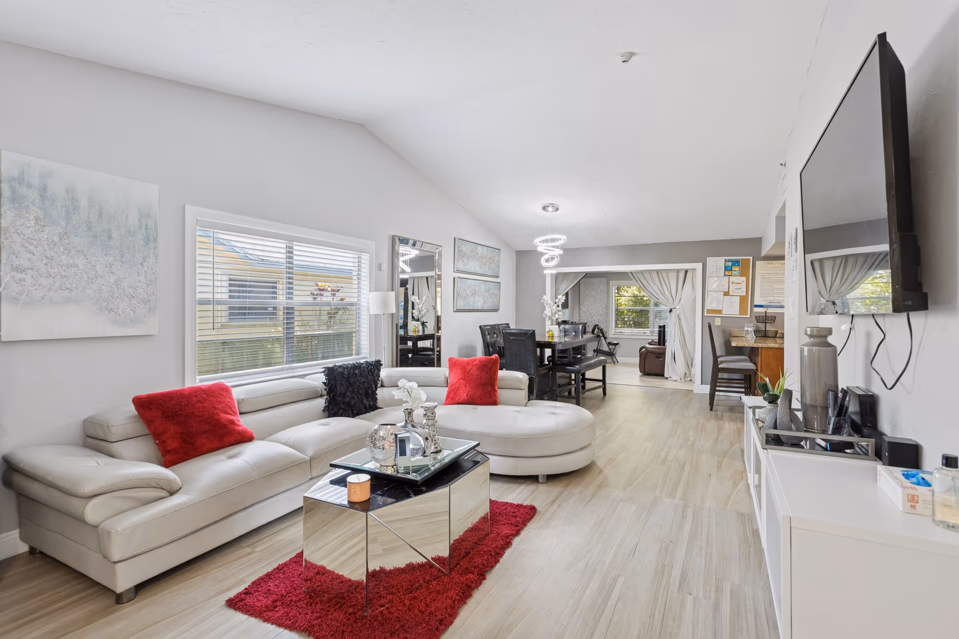Bright, modern living area with white sectional sofa, red pillows, and a glass coffee table.
