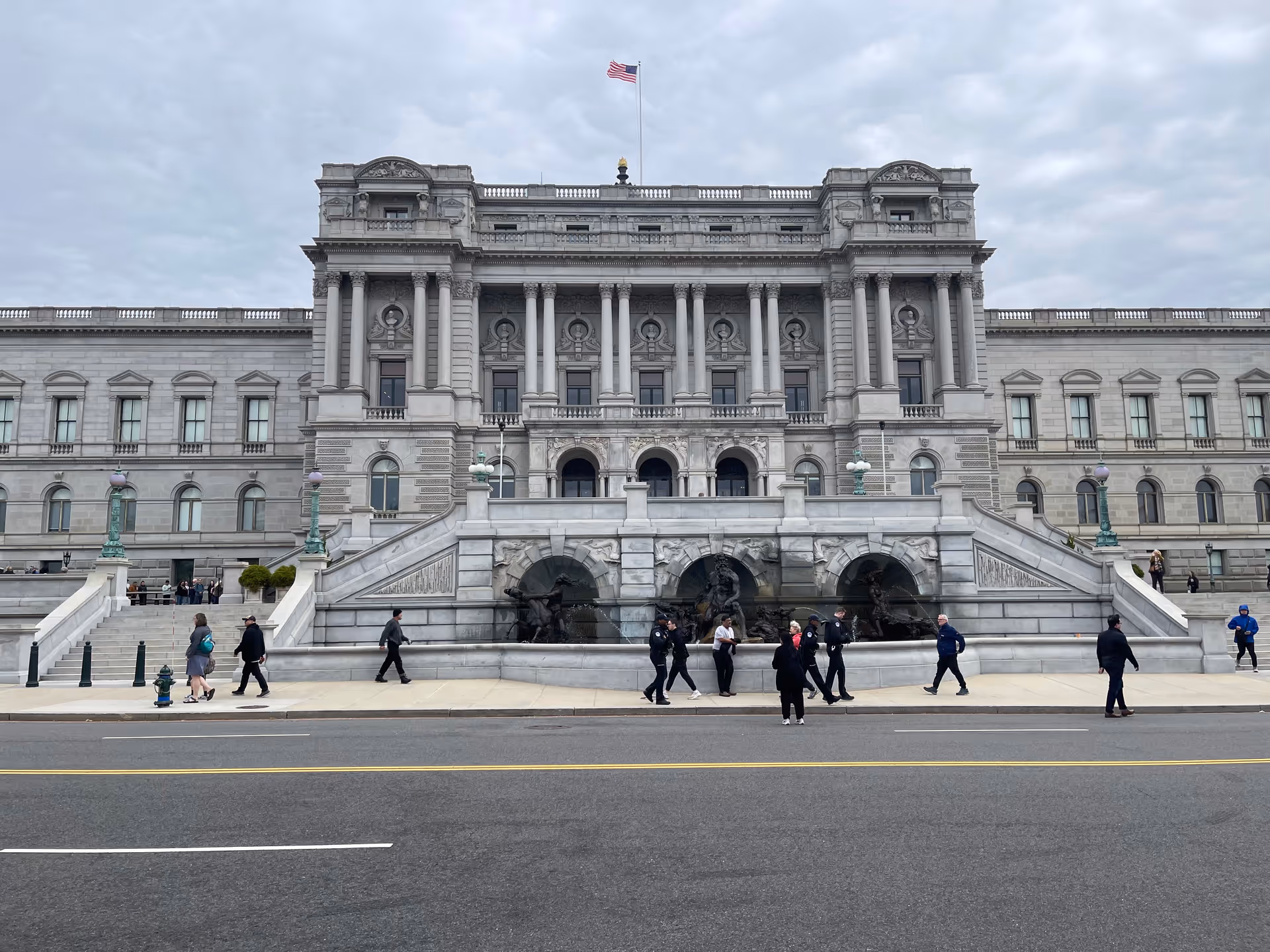Front view of a grand historic building with wide stairs and pedestrians along the street.