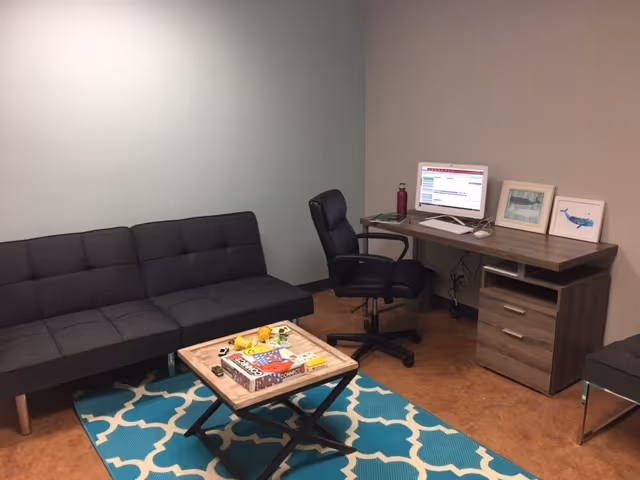A small living area with a gray sofa, coffee table, rug, and a desk with computer.