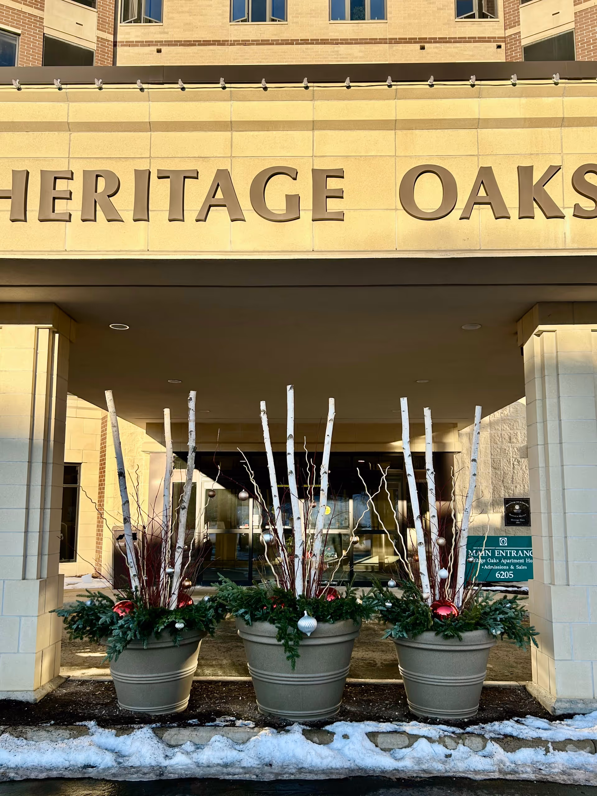 Front entrance of Heritage Oaks with decorative planters and bare trees in snow.
