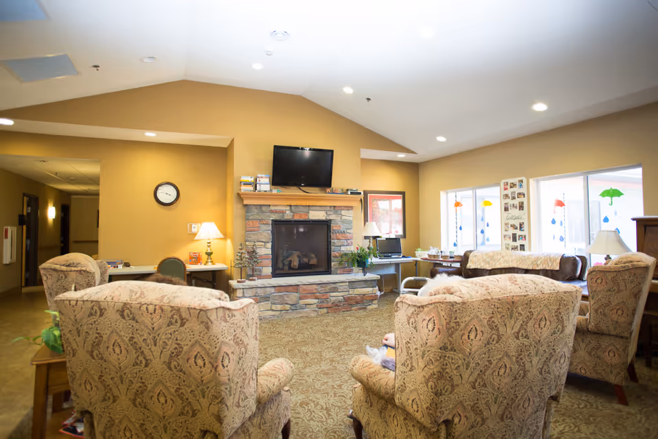 Cozy senior living lounge with a stone fireplace, sofas, chairs, and a mounted TV.