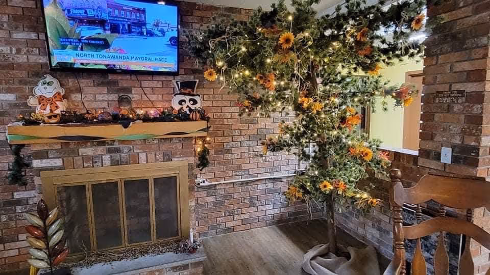 Cozy brick fireplace with a mounted TV, decorative tree, and holiday lights in a living room.