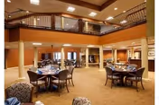 A warmly lit senior living dining room with round tables and seating.
