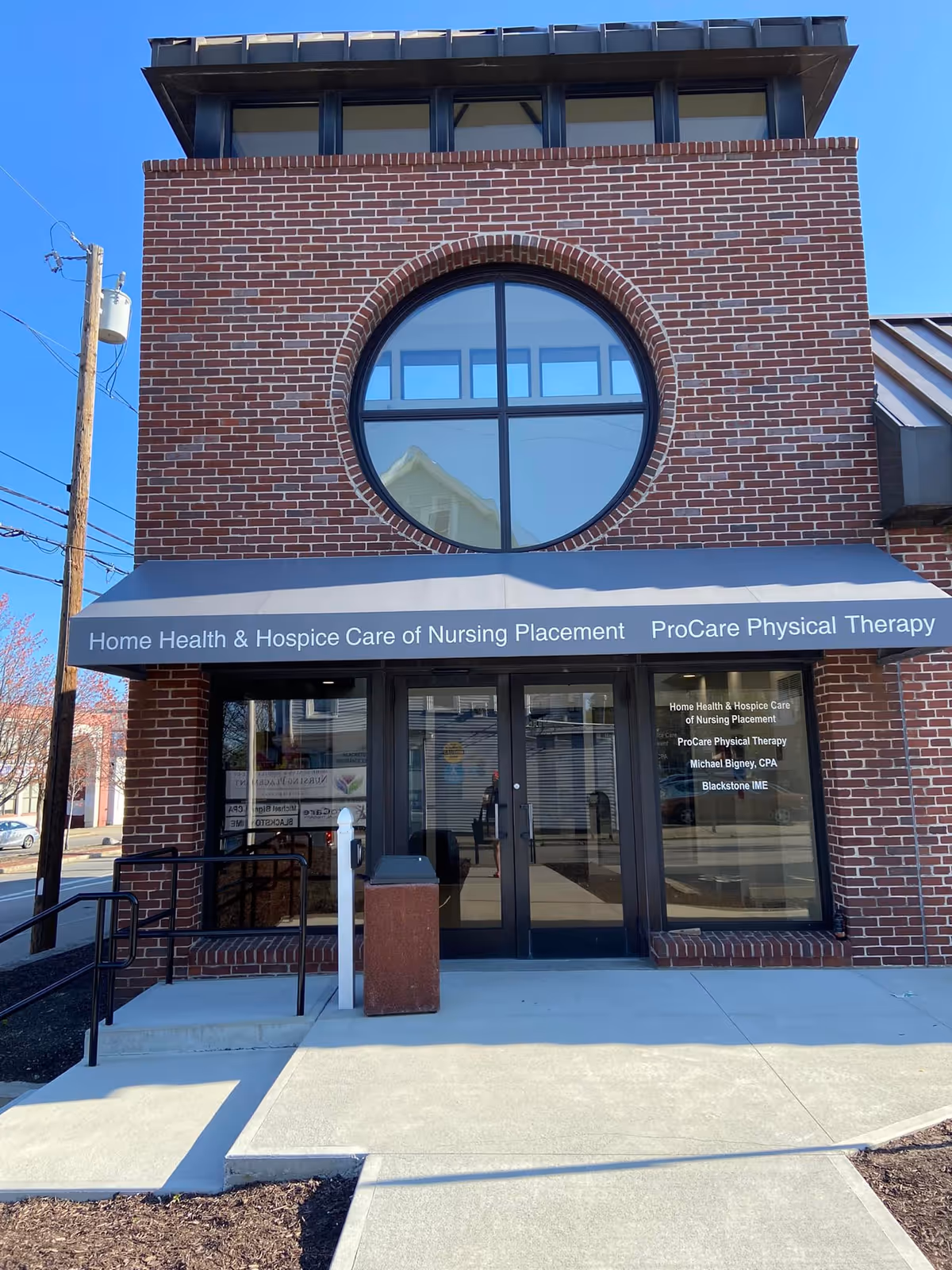 Brick building storefront with circular window and blue awning showing facility name.