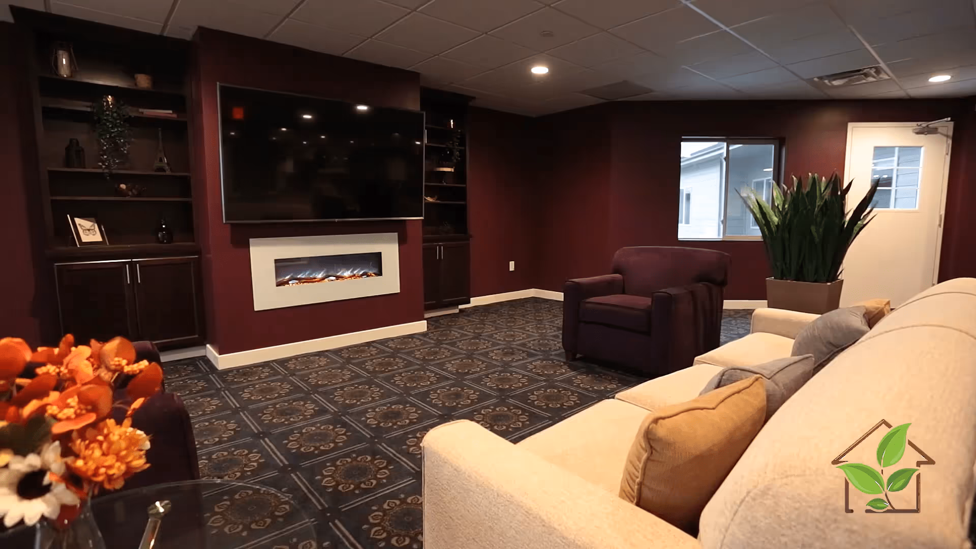 A cozy lounge with a sofa and armchair facing a wall-mounted TV and built-in electric fireplace.