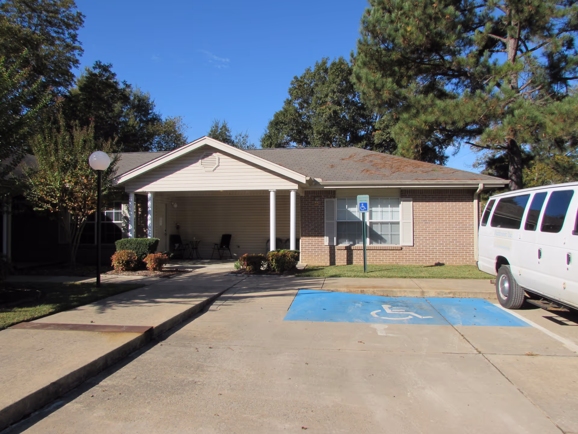 Single-story brick senior living facility with a covered entrance, handicap parking, and a white van.