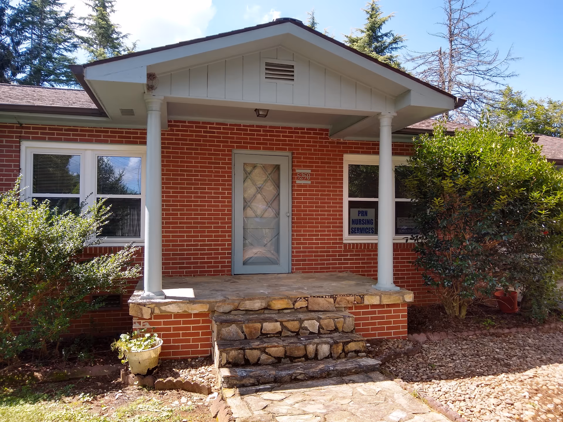 Brick nursing facility entrance with stone steps, white porch columns, and window sign.