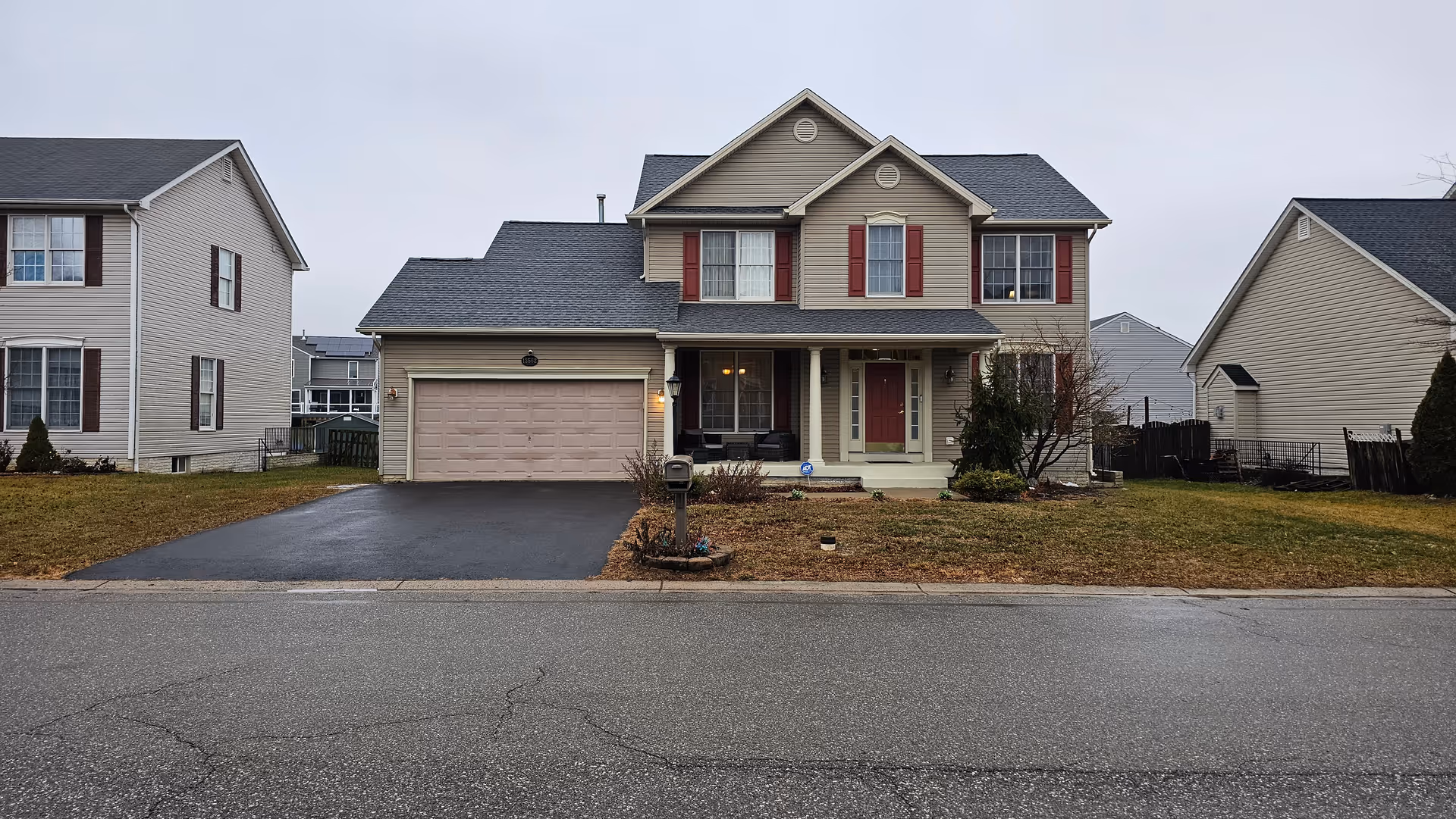 Two-story beige suburban house with a two-car garage and front yard.
