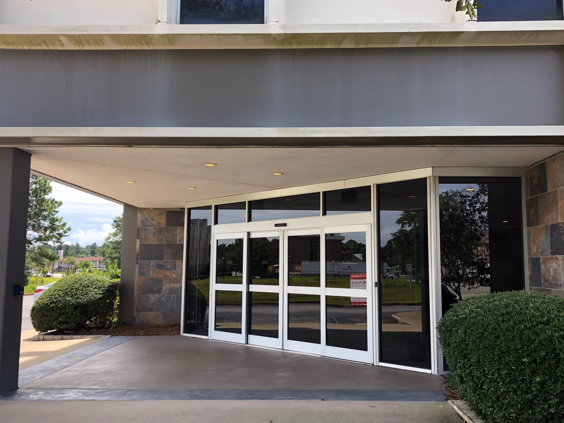Exterior entrance to a senior living facility with glass doors and landscaping.